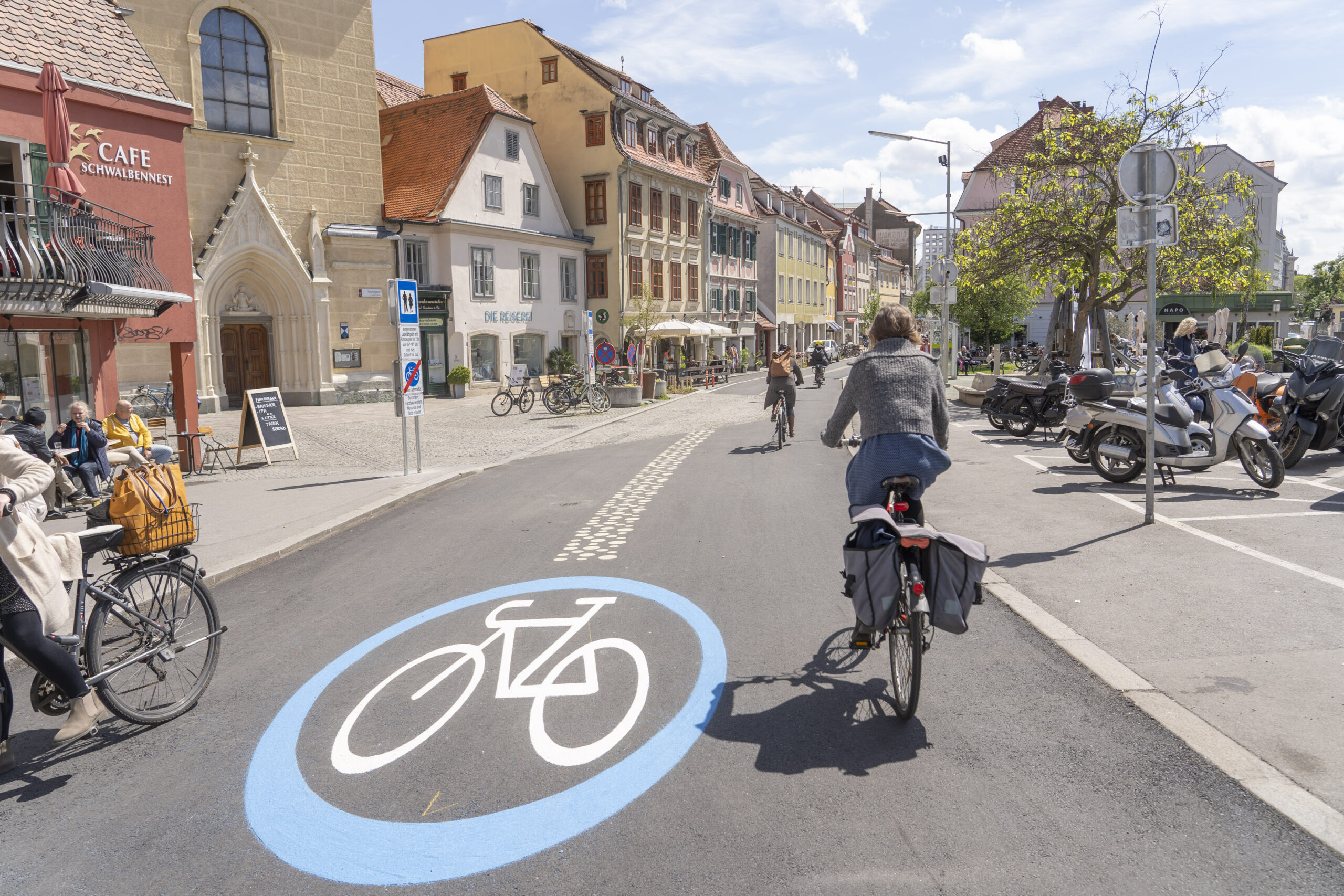 Die Fahrradstraße Neutorgasse in Graz mit Radfahrenden und einer große Bodenmarkierung fürs Radfahren.